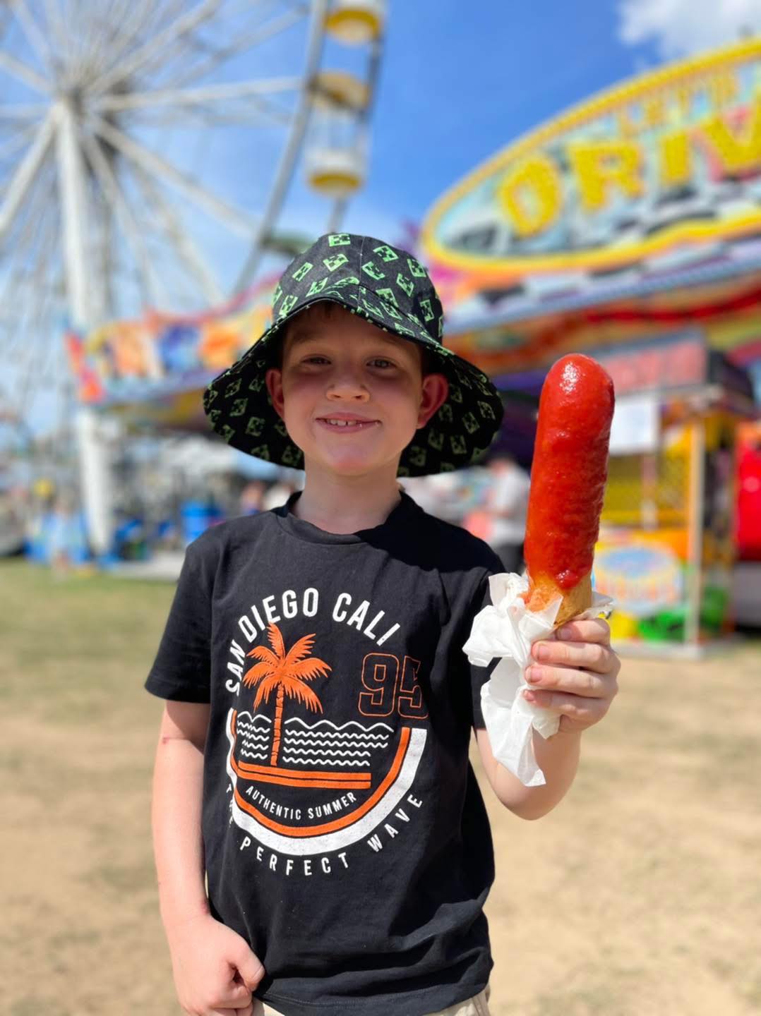 Boy enjoying dagwood dog at school fete with ferris wheel